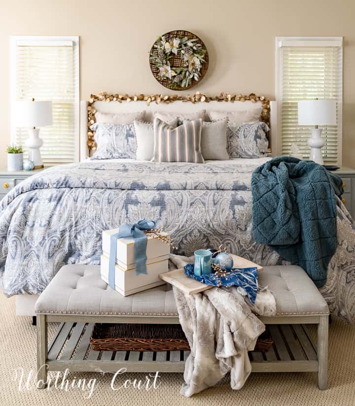 Christmas gifts on a bench at foot of the bed with a tray with coffee mug and blue ornaments and a fur throw blanket