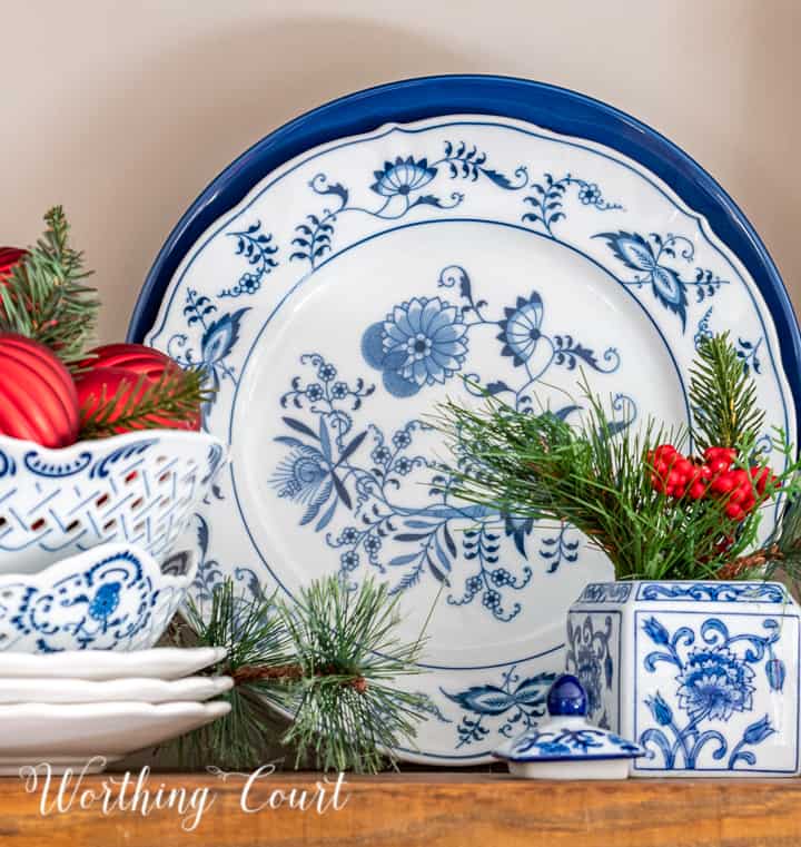 Blue and white dishes with faux greenery and red berries displayed on a wood shelf.