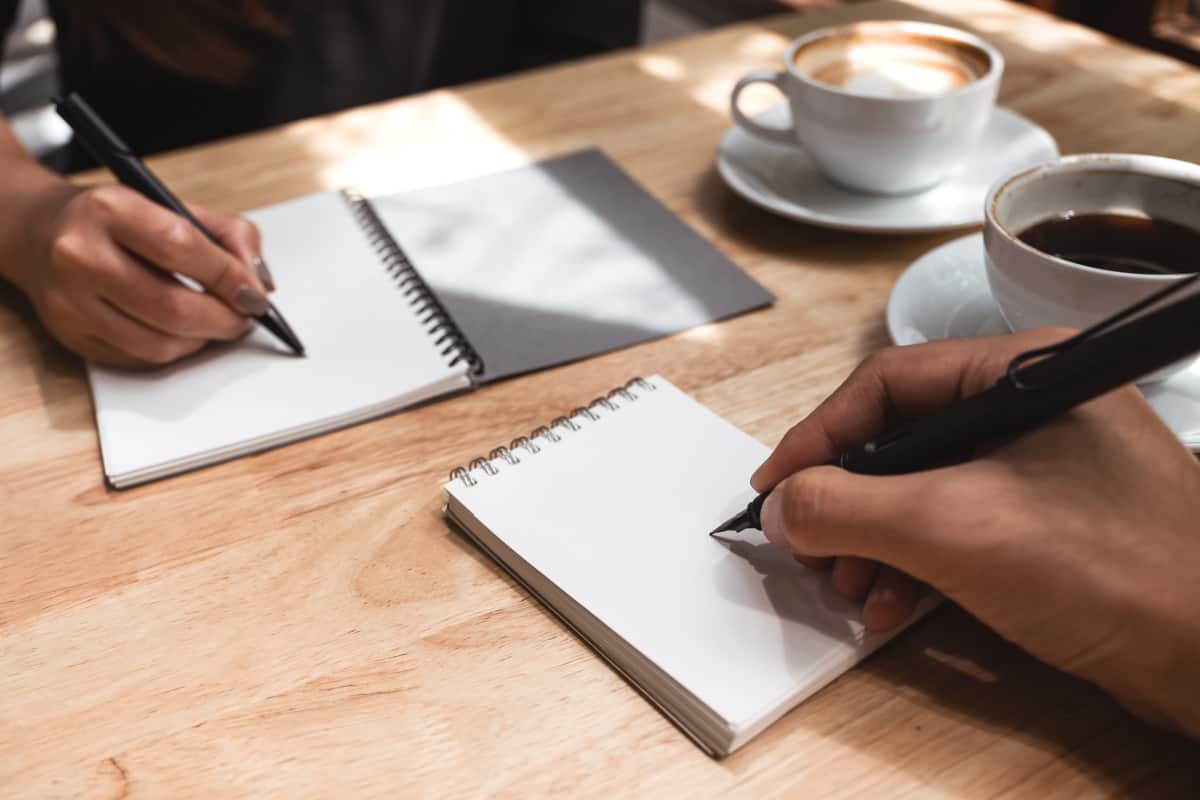 the hands of two people writing on paper pads