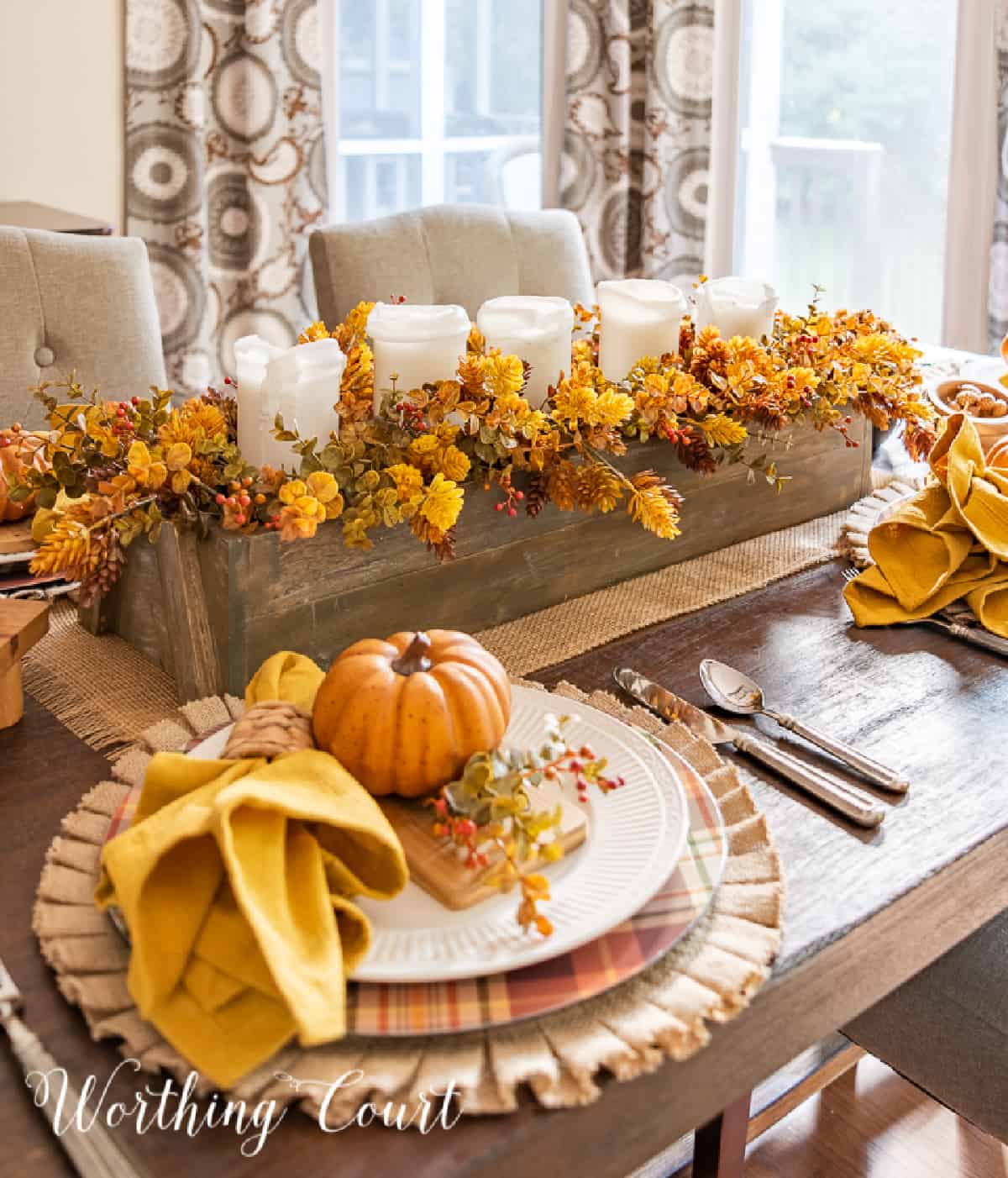 Thanksgiving place setting with a burlap placemat, plaid charger, white dinner plate and fall accessories.