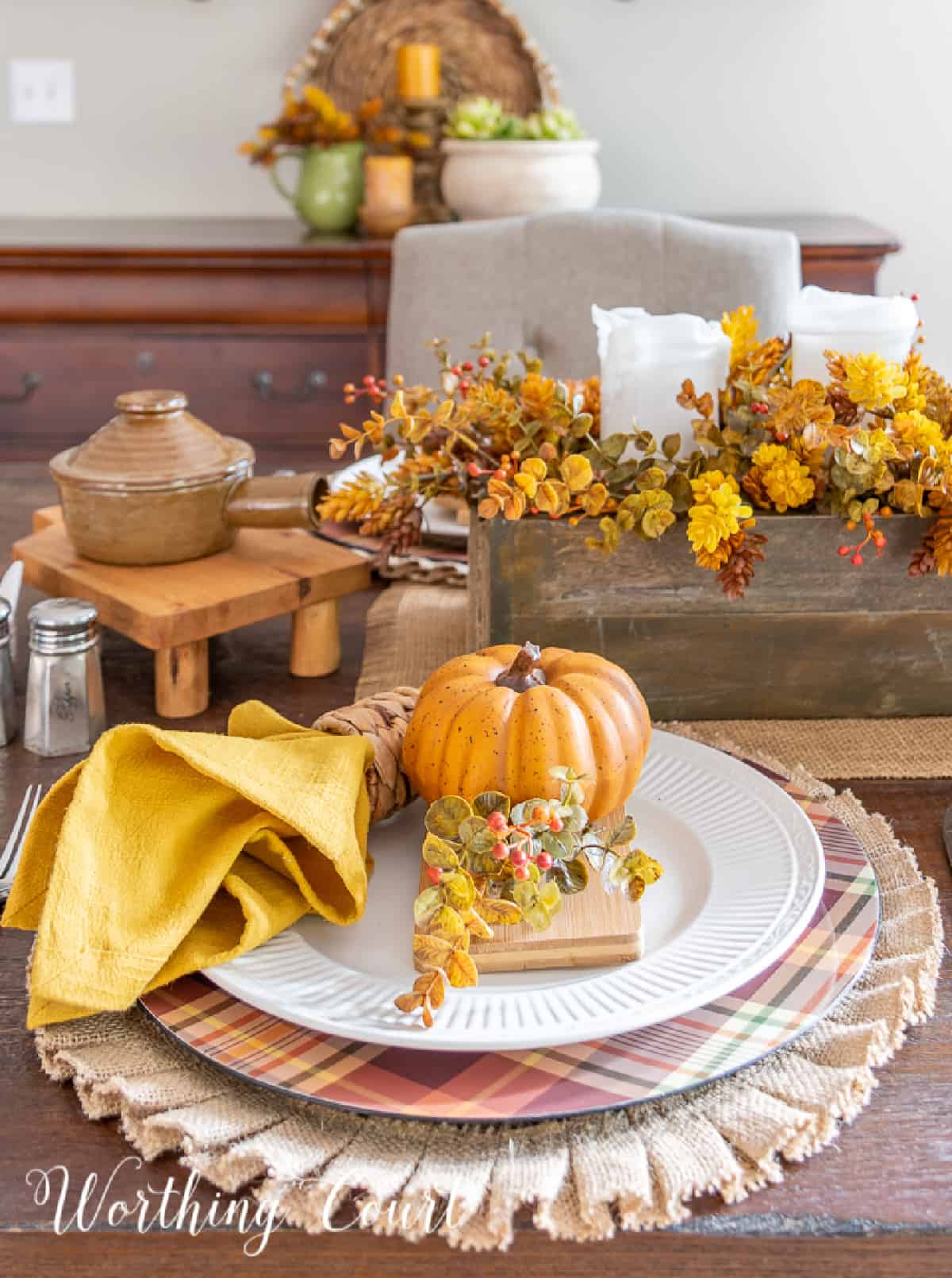 Thanksgiving place setting with a burlap placemat, plaid charger, white dinner plate and fall accessories.