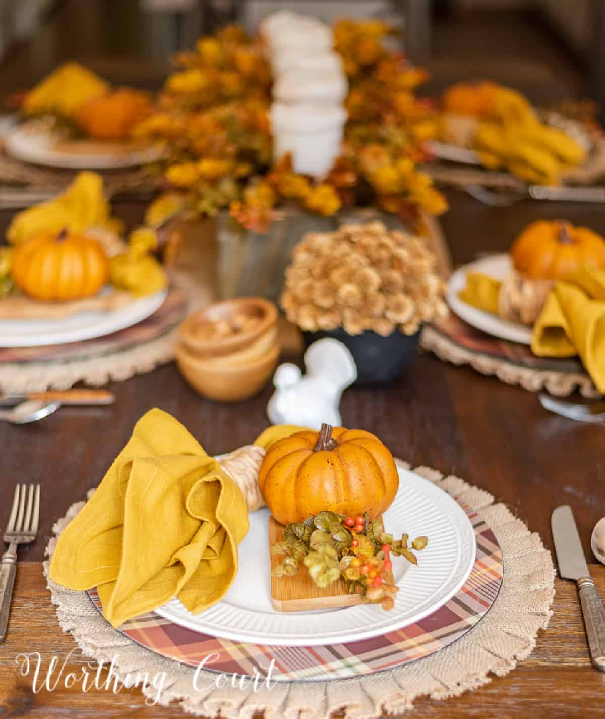 Thanksgiving place setting with a burlap placemat, plaid charger, white dinner plate and fall accessories.