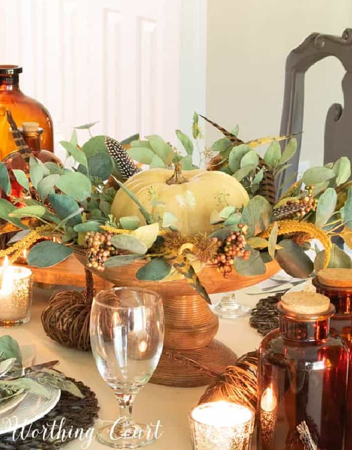 white pumpkin in a wooden pedestal bowl surround by faux eucalyptus