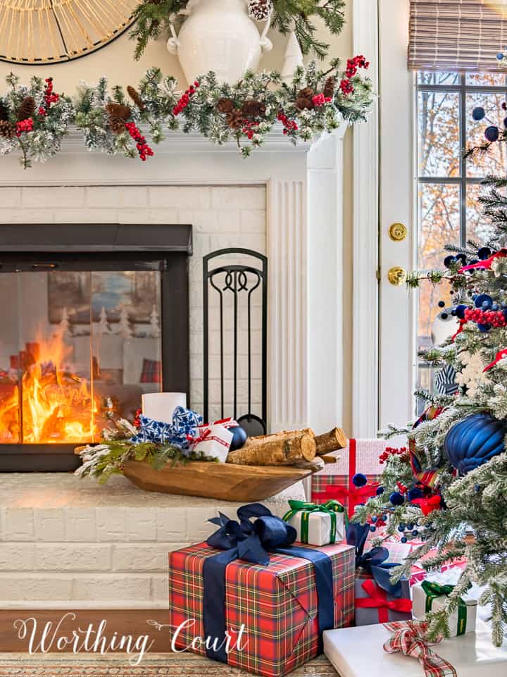 blue and red plaid wrapped Christmas gift beside tree and fireplace