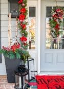 front porch decorated for Christmas with red and white garland, planters, trees, lanterns, rugs and pillows