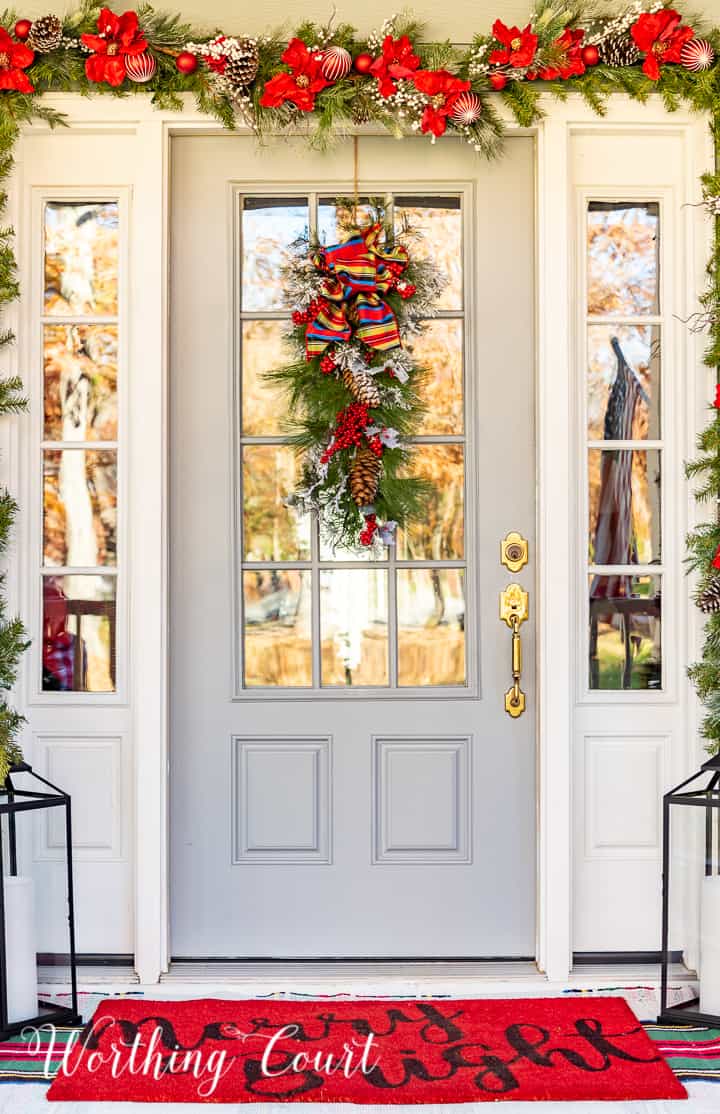 front porch decorated for Christmas with red and white garland, planters, trees, lanterns, rugs and pillows