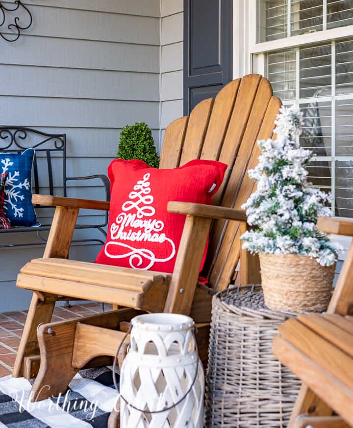 front porch decorated for Christmas with red and white garland, planters, trees, lanterns, rugs and pillows