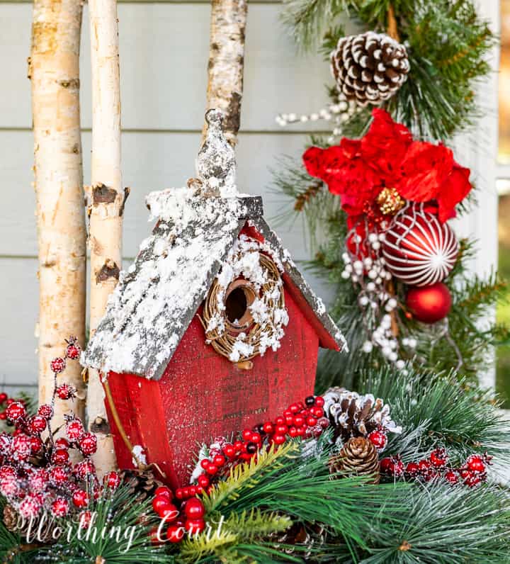 front porch decorated for Christmas with red and white garland, planters, trees, lanterns, rugs and pillows