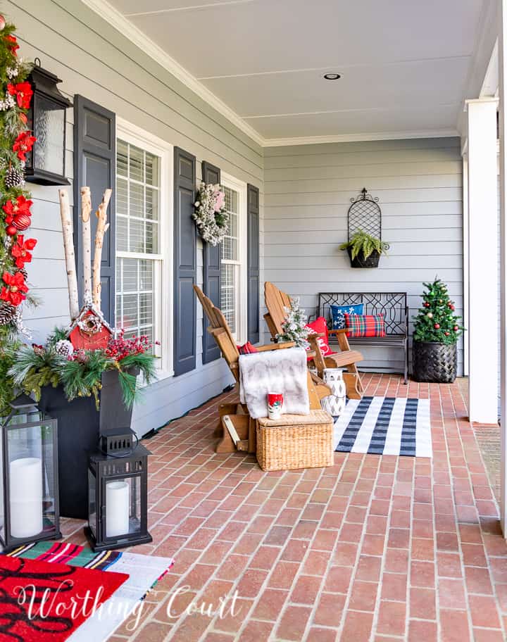 front porch decorated for Christmas with red and white garland, planters, trees, lanterns, rugs and pillows