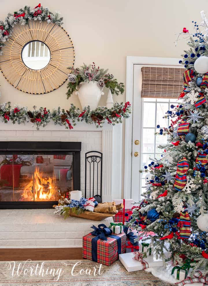 Fireplace decorated for Christmas with a garland and blue, red and white decorations sitting beside Christmas tree