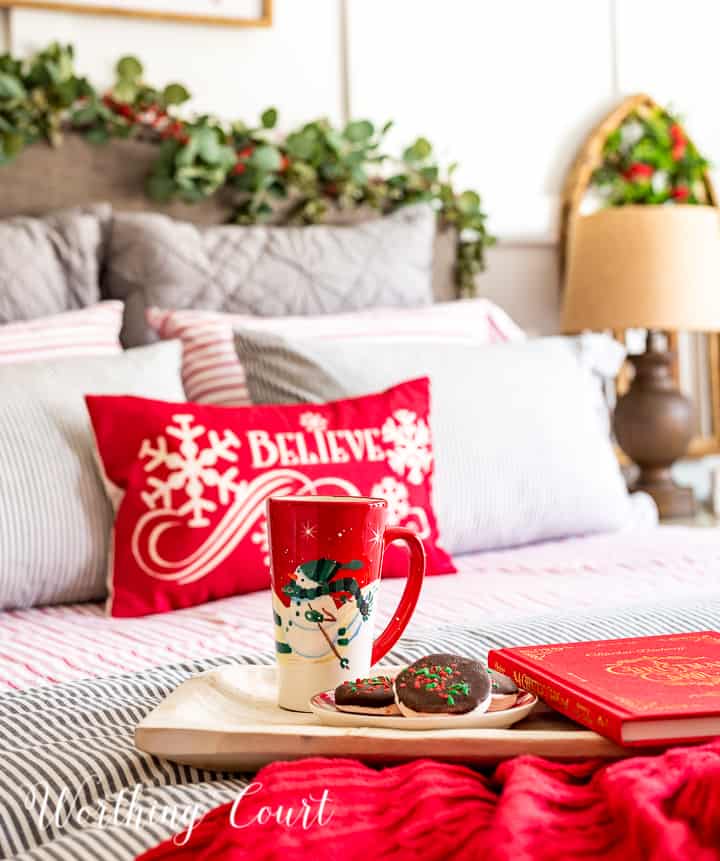 bed with red Christmas pillow and wood tray on top of a red throw blanket