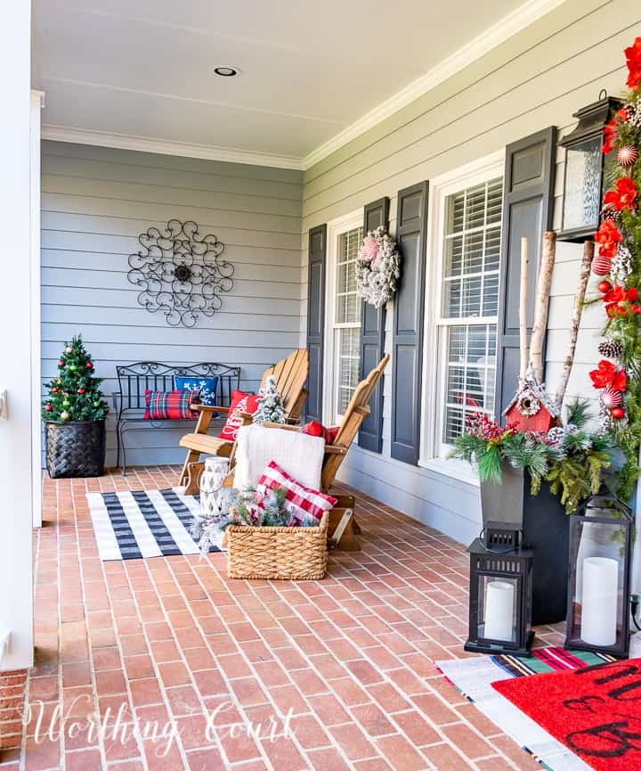 front porch decorated for Christmas with red and white garland, planters, trees, lanterns, rugs and pillows