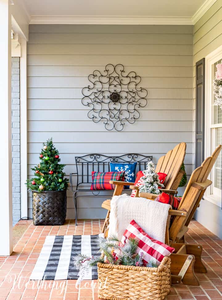 front porch decorated for Christmas with red and white garland, planters, trees, lanterns, rugs and pillows