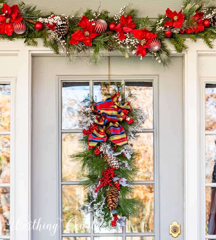 front porch decorated for Christmas with red and white garland, planters, trees, lanterns, rugs and pillows