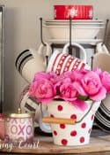 Valentine's day vignette with tiered mug tree and assorted red, white and pink accessories on a round bread board