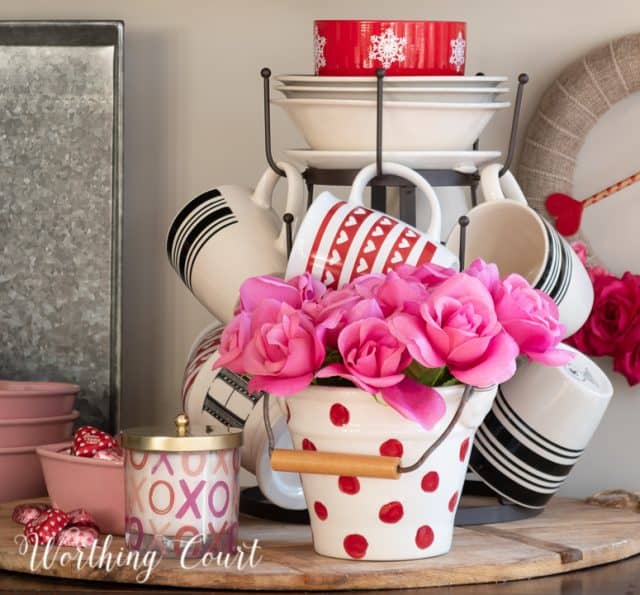 Valentine's day vignette with tiered mug tree and assorted red, white and pink accessories on a round bread board
