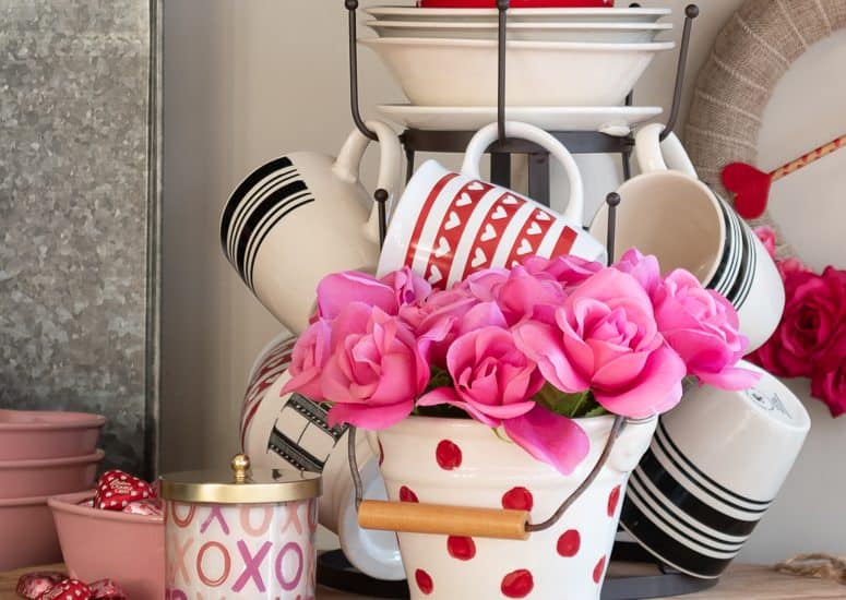 Valentine's day vignette with tiered mug tree and assorted red, white and pink accessories on a round bread board