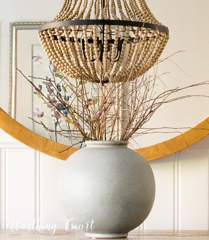 gray vase filled with bare branches in front of round mirror on sideboard