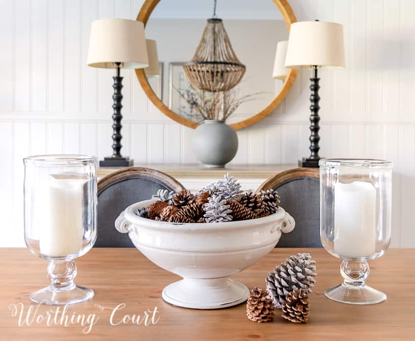 white pedestal bowl filled with pinecones and glass candle holders on wood dining table