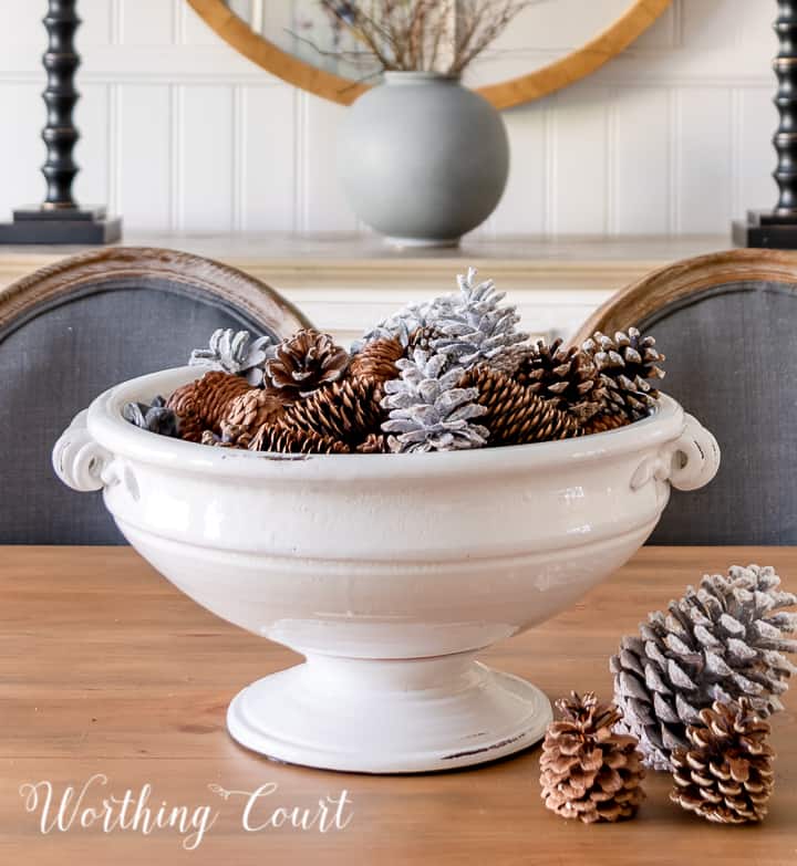 white pedestal bowl filled with pinecones on wood dining table