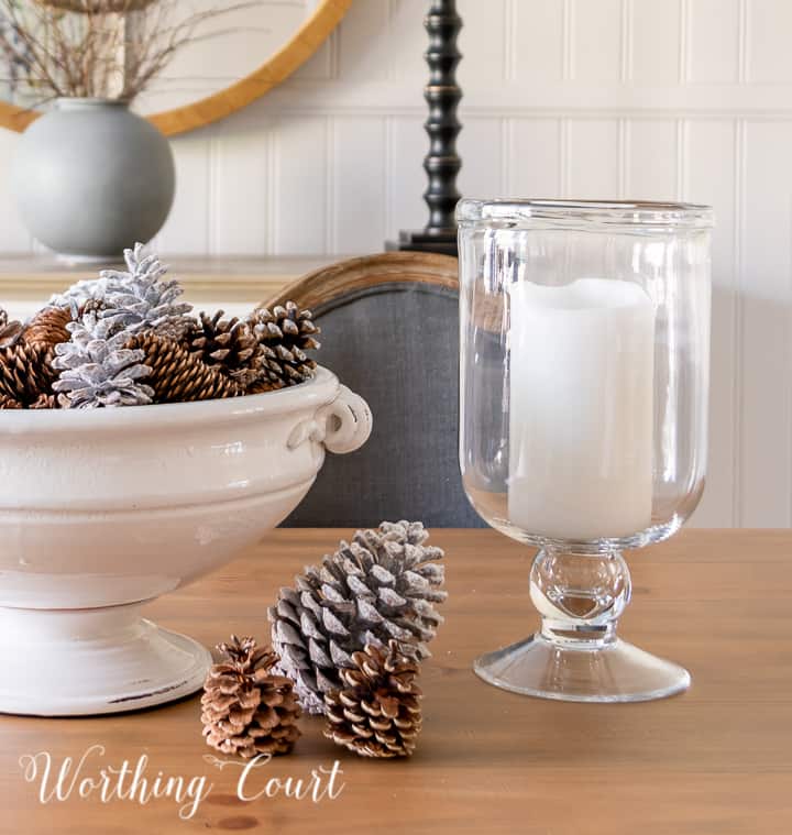 white pedestal bowl filled with pinecones and glass candle holders on wood dining table