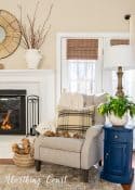 light gray recliner and blue side table beside white brick fireplace with winter decor
