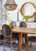 transitional style cottage dining room with white sideboard, round mirror, natural wood table and oval back chairs