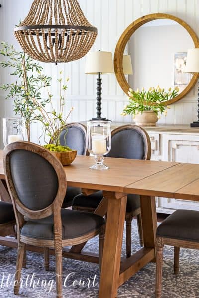 transitional style cottage dining room with white sideboard, round mirror, natural wood table and oval back chairs