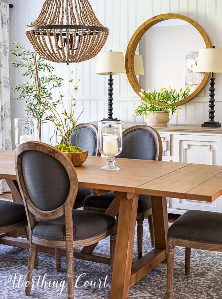 transitional style cottage dining room with white sideboard, round mirror, natural wood table and oval back chairs