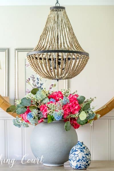 faux flower arrangement in front of a round mirror above a dining room sideboard