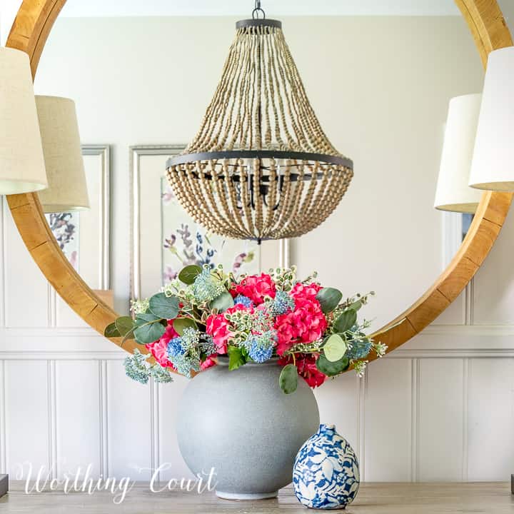 faux flower arrangement in front of a round mirror above a dining room sideboard