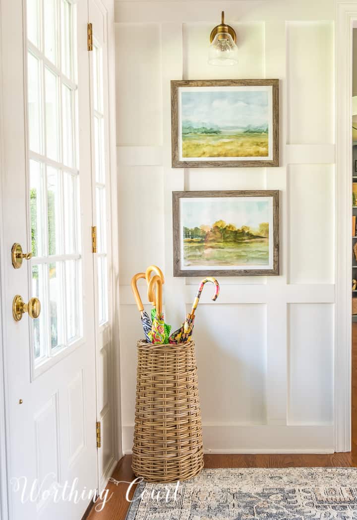 basket umbrella stand with assorted umbrellas in a foyer with white walls