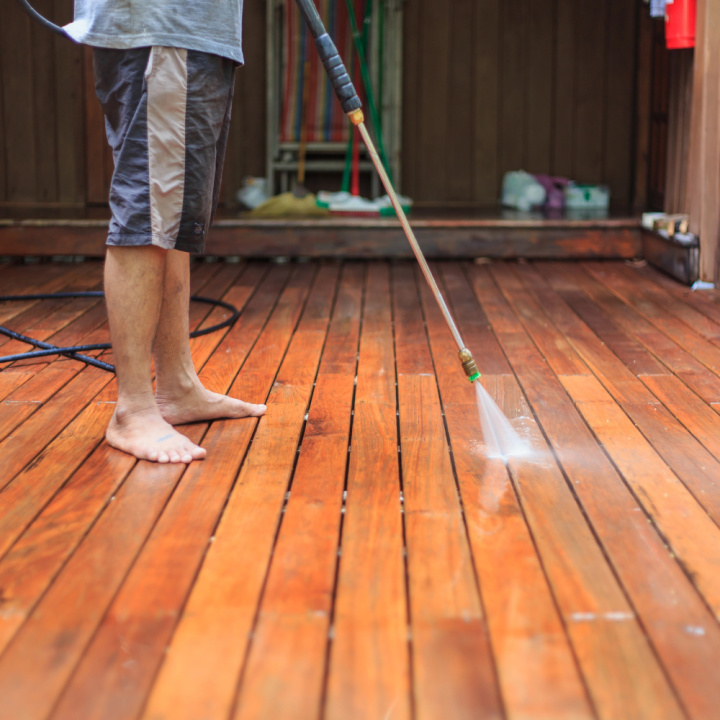 person pressure washing a wood deck