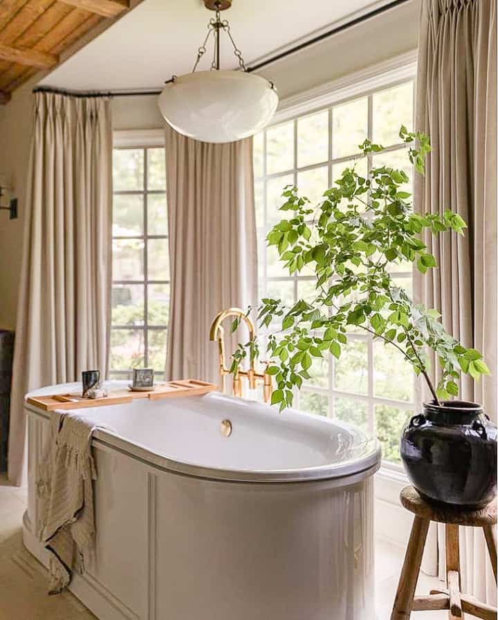 free standing oval bathtub in front of a large window