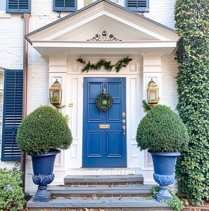 small front porch on a white house with greenery and flowers and a blue door
