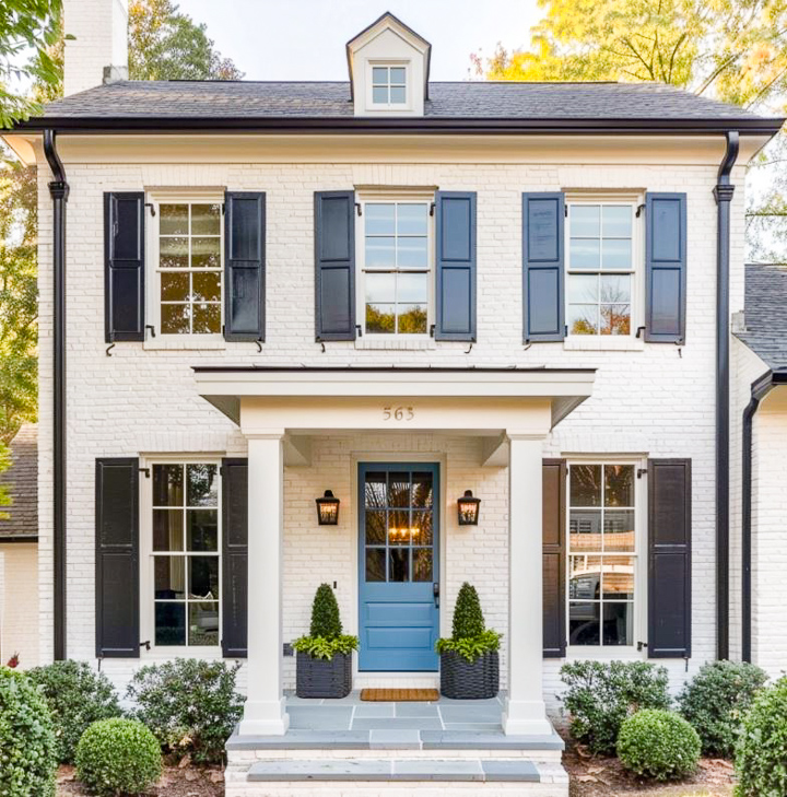 small front porch on a white house with greenery and flowers and a blue door