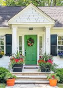 small front porch on white house with black shutters and window boxes with a green front door flanked by pots of flowers