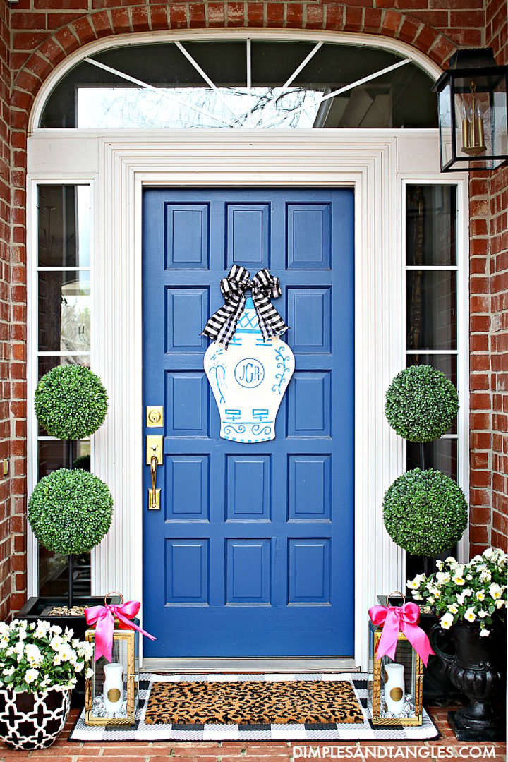 small front porch on a red brick house with a blue door flanked with topiaries