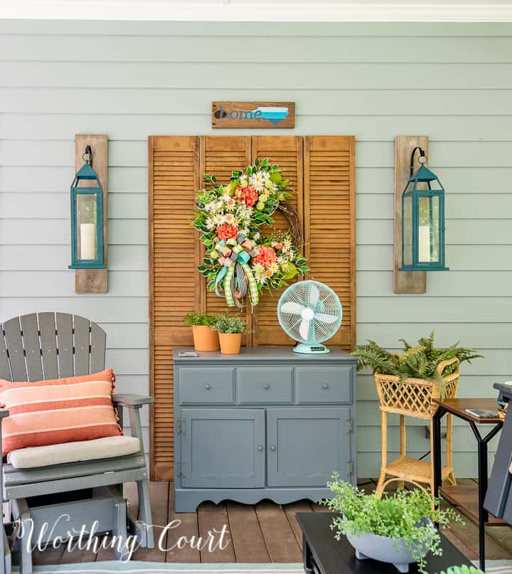Gray chest with a wreath hanging above it on old bifold doors, flanked by a glider and a plant stand
