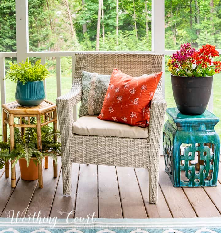 Arm chair, pillows, small tables and plants on a screen porch