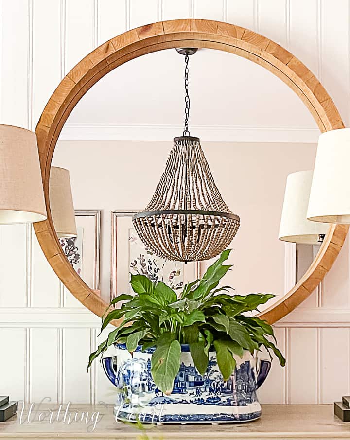 Dining room sideboard with round mirror, buffet lamps and blue and white urn filled with a plant