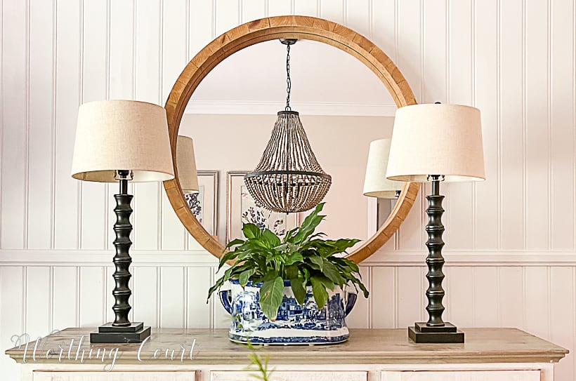 Dining room sideboard with round mirror, buffet lamps and blue and white urn filled with a plant