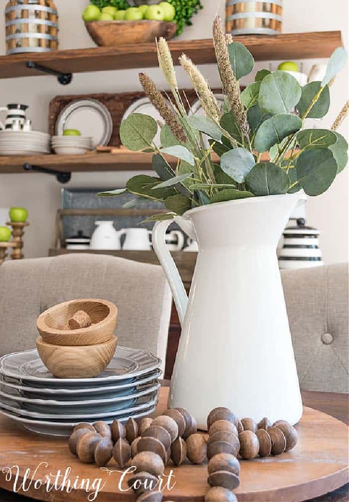 table centerpiece with a white pitcher and eucalyptus leaves and wood beads