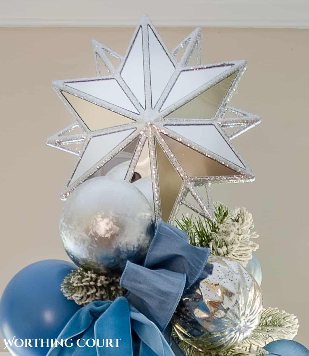 flocked Christmas tree decorated with French blue and silver ornaments and ribbon topped with a mirrored silver star