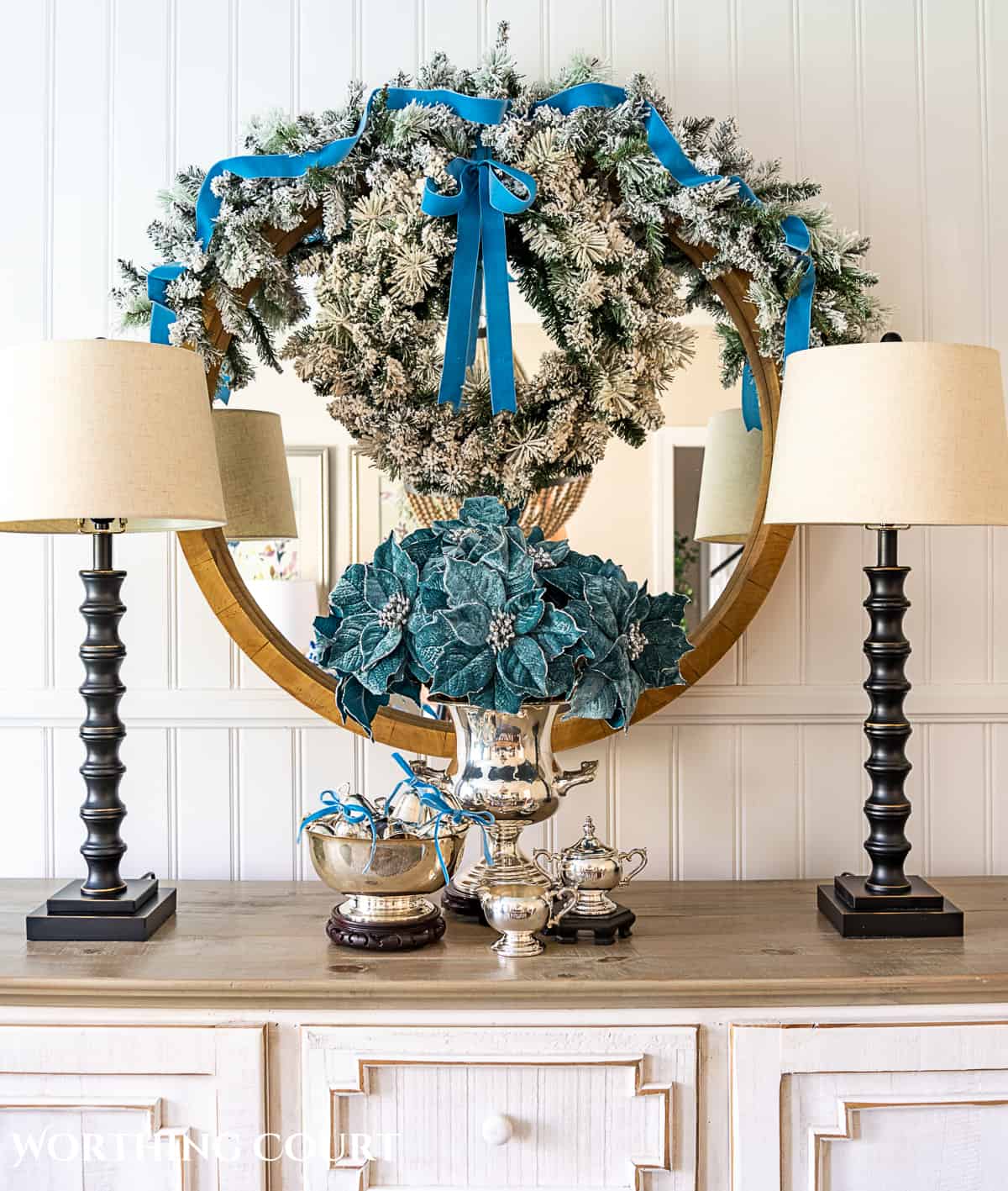 sterling silver champagne bucket and paul revere bowl with French blue Christmas decorations in front of a round mirror above a sideboard