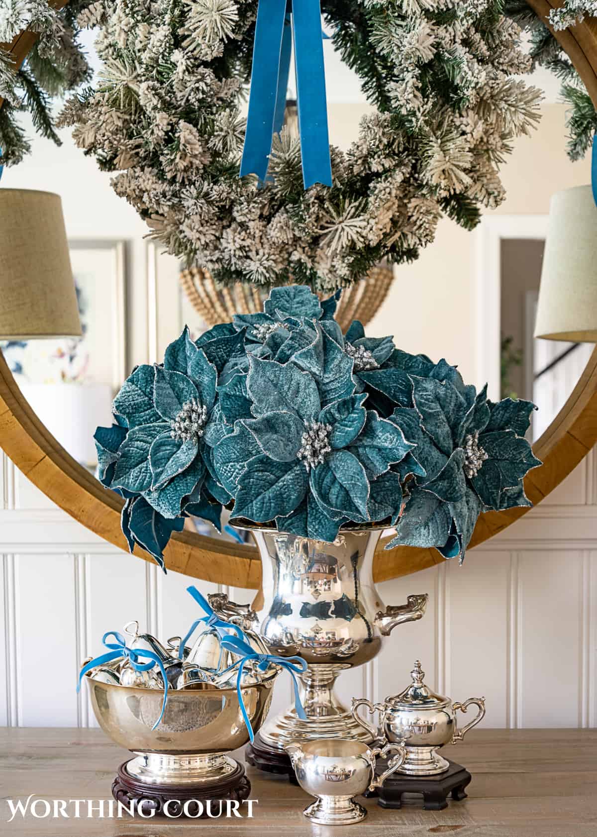 sterling silver champagne bucket and paul revere bowl with French blue Christmas decorations in front of a round mirror above a sideboard