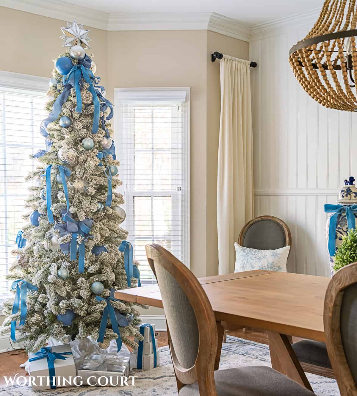 flocked Christmas tree in a bay window decorated with French blue and silver ornaments and ribbon