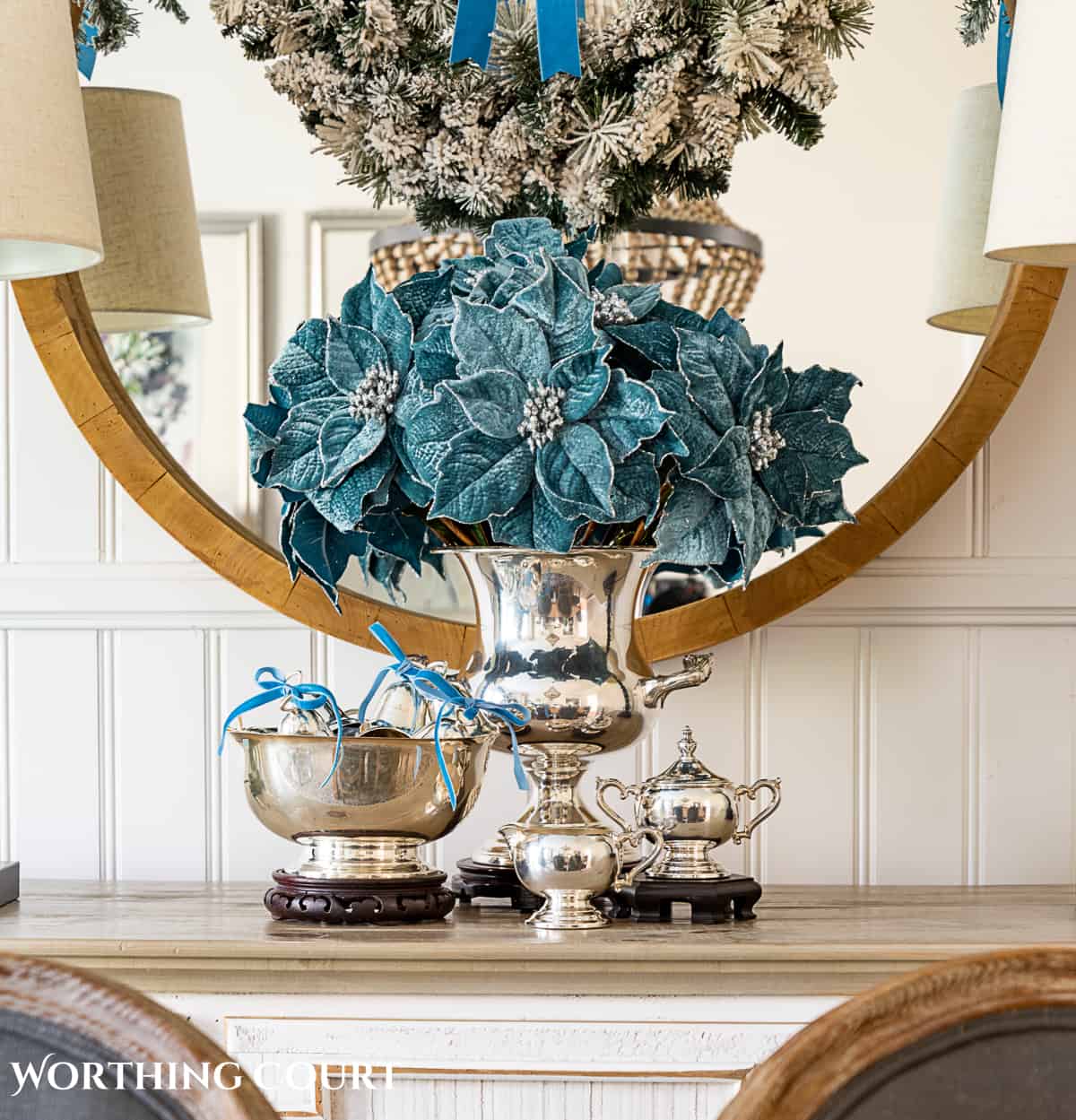 sterling silver champagne bucket and paul revere bowl with French blue Christmas decorations in front of a round mirror above a sideboard