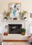 white brick fireplace with art above and a decorated mantle.