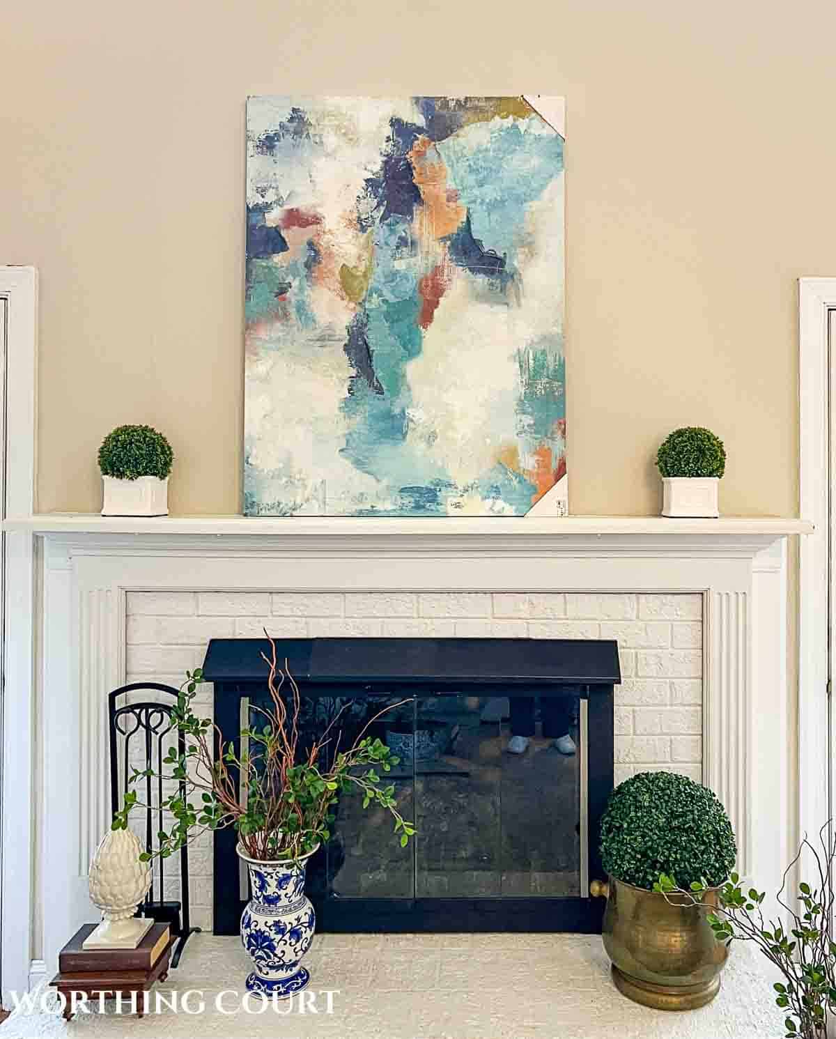 abstract canvas art sitting on the mantel above a white brick fireplace